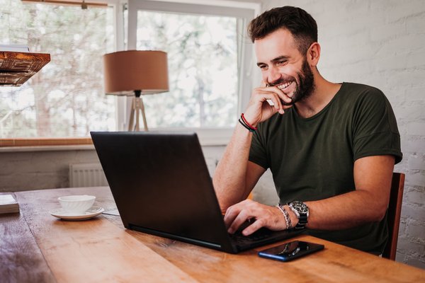 Mann lächelt, während er einen Laptop benutzt.